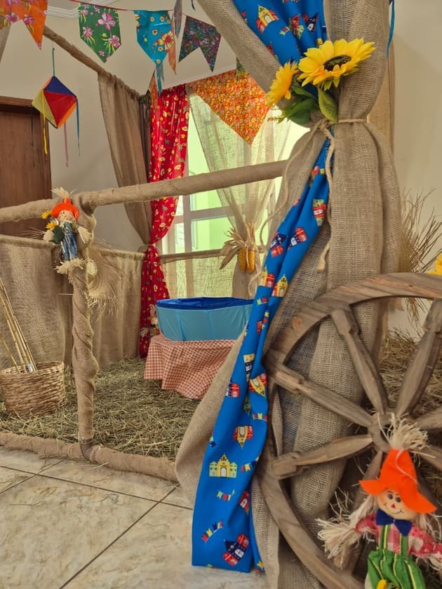 Decoração de festa junina com roda de carroça, tecido rústico e bandeirinhas coloridas