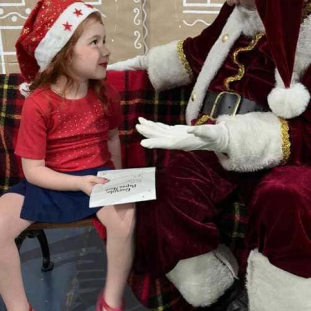 Papai Noel com barba natural conversando com uma criança durante uma ação de Natal