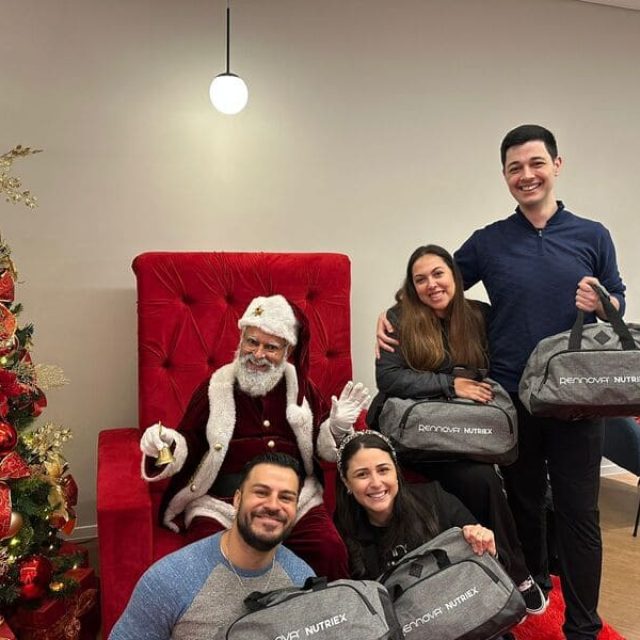 Papai Noel sentado em poltrona vermelha acompanhado por convidados durante evento de Natal