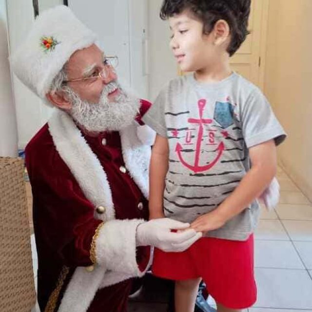 Papai Noel com barba natural conversando com uma criança durante visita de Natal em residência